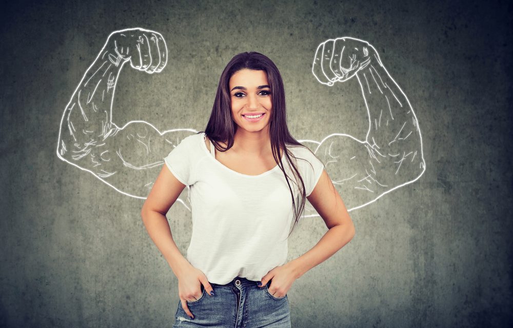 Strong happy young woman flexing her muscles on gray background